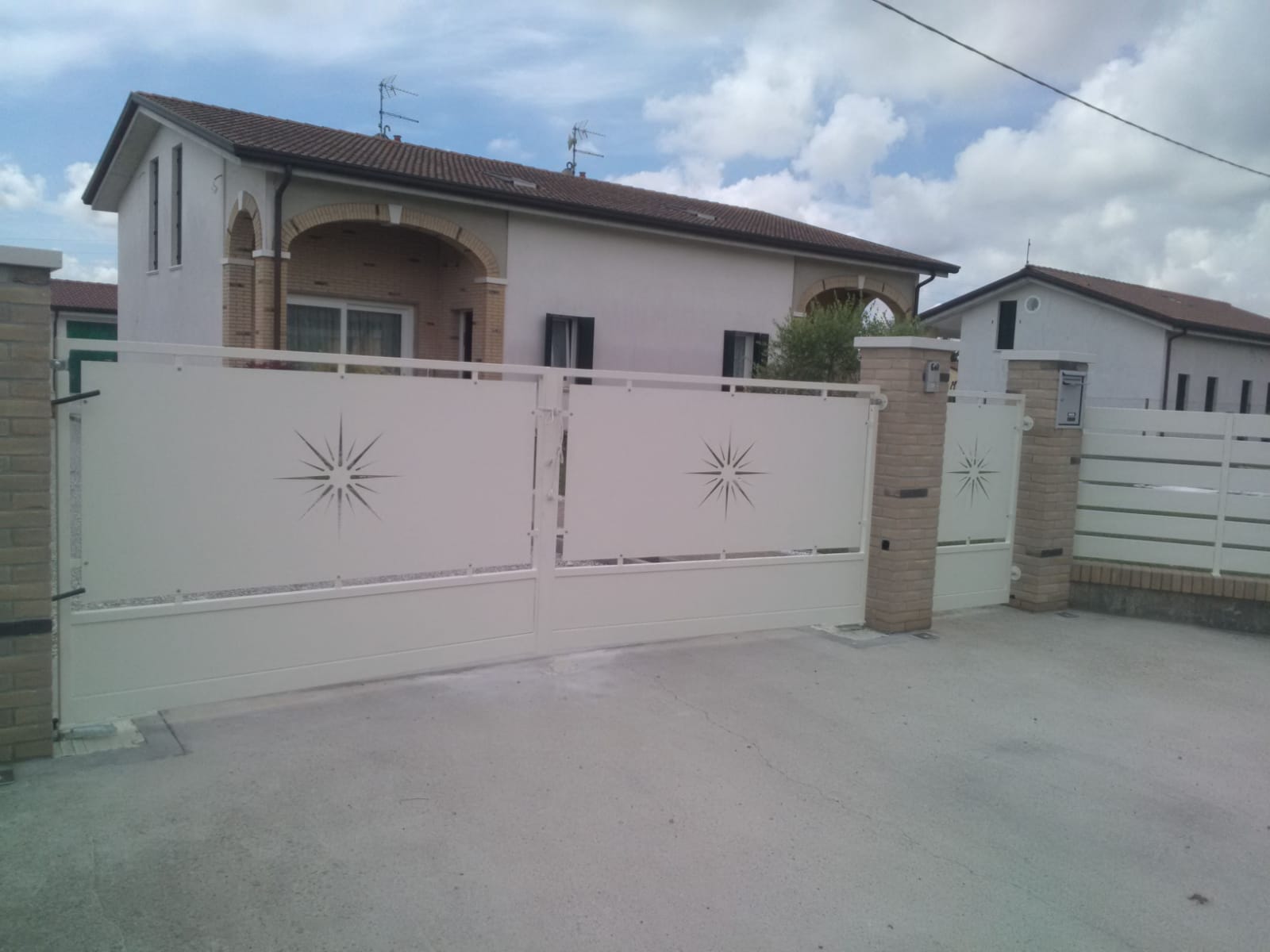 Cancello d'accesso in metallo bianco con ritagli a forma di stella davanti a una casa di colore chiaro.
