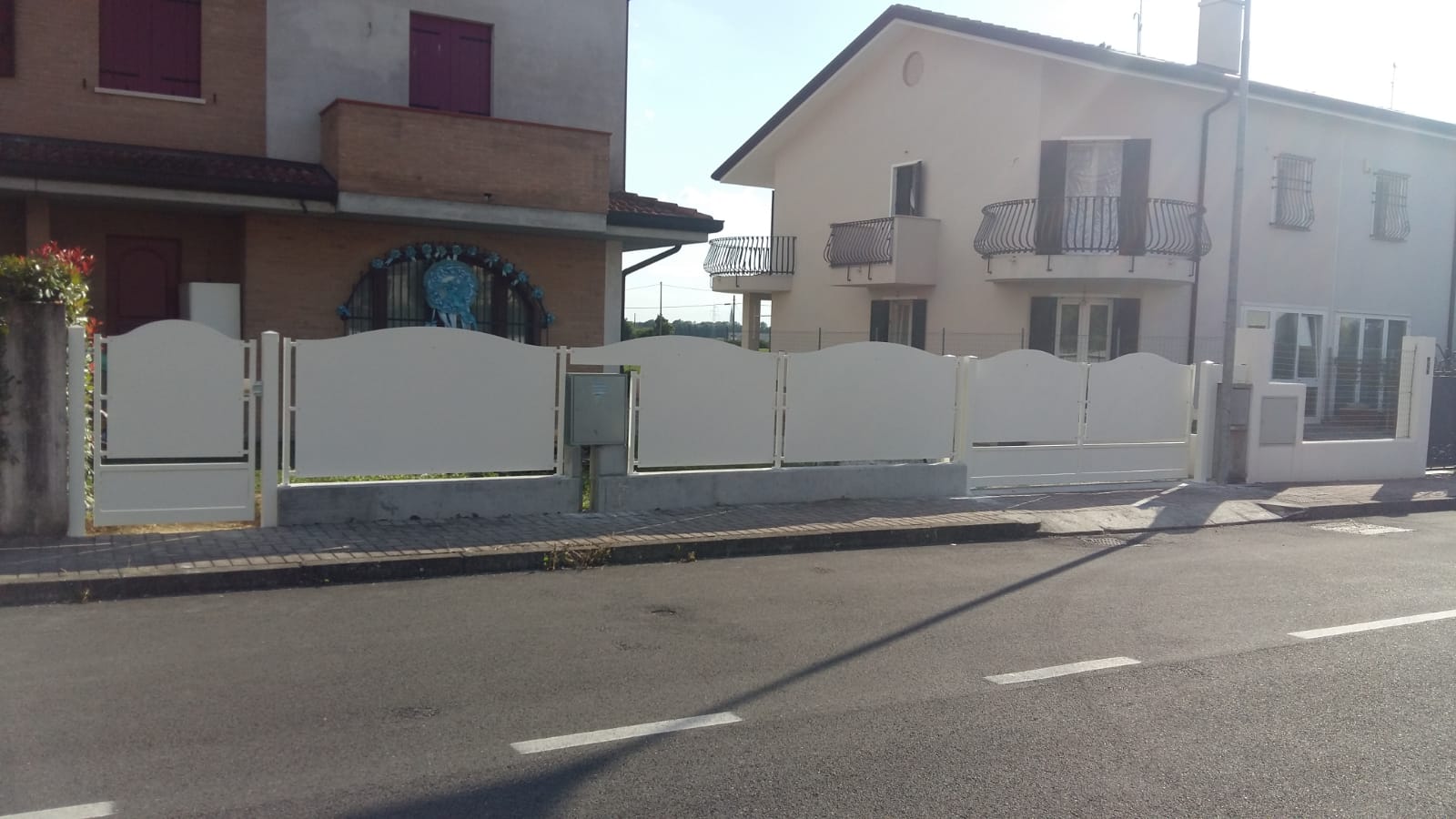 Recinzione in metallo bianco davanti a case a due piani su una strada.