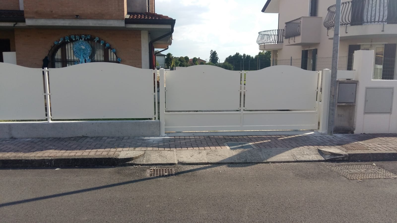 Cancello carrabile in metallo bianco su una strada asfaltata di fronte a una casa.