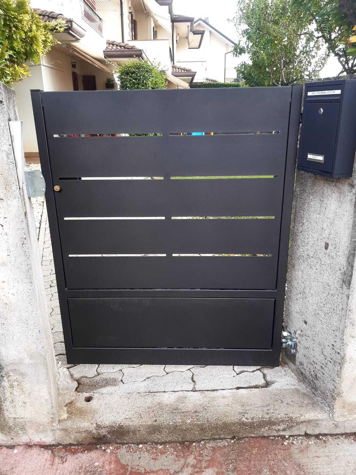 Cancello in metallo nero con fessure orizzontali, montato su un muro di cemento, accanto a una cassetta postale nera.
