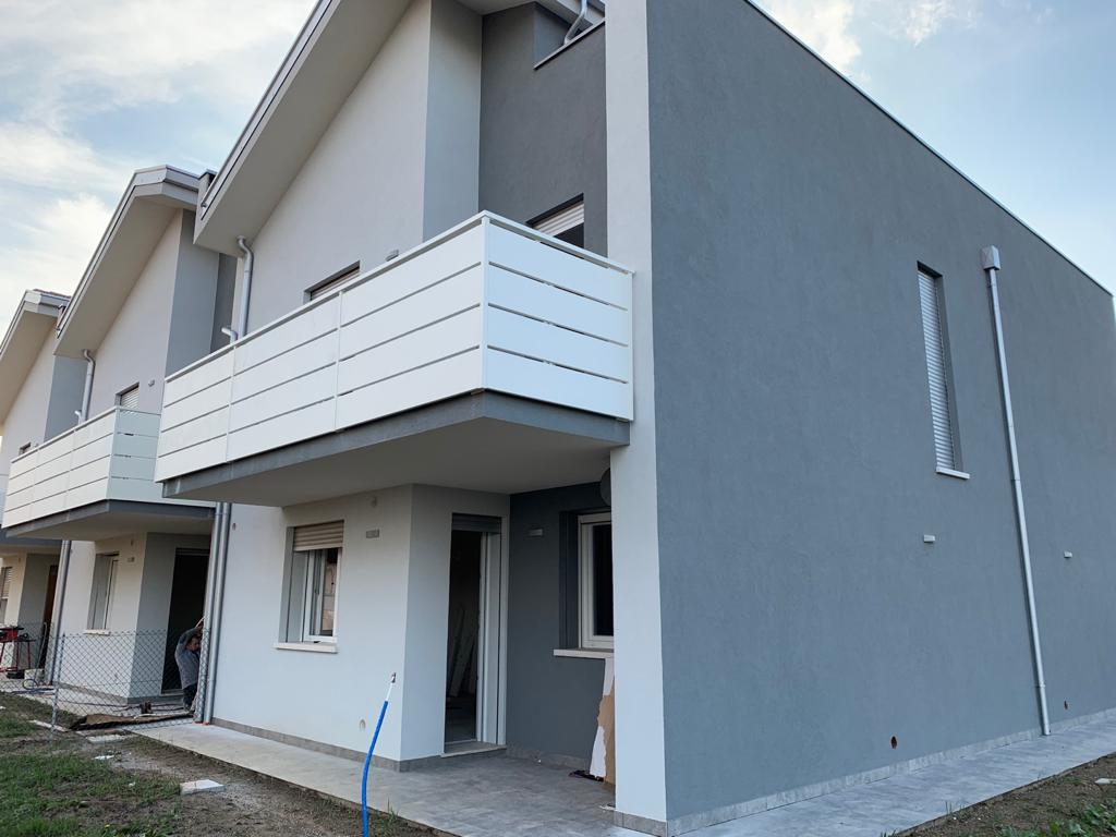 Case a schiera grigie e bianche con balconi, sotto un cielo nuvoloso.