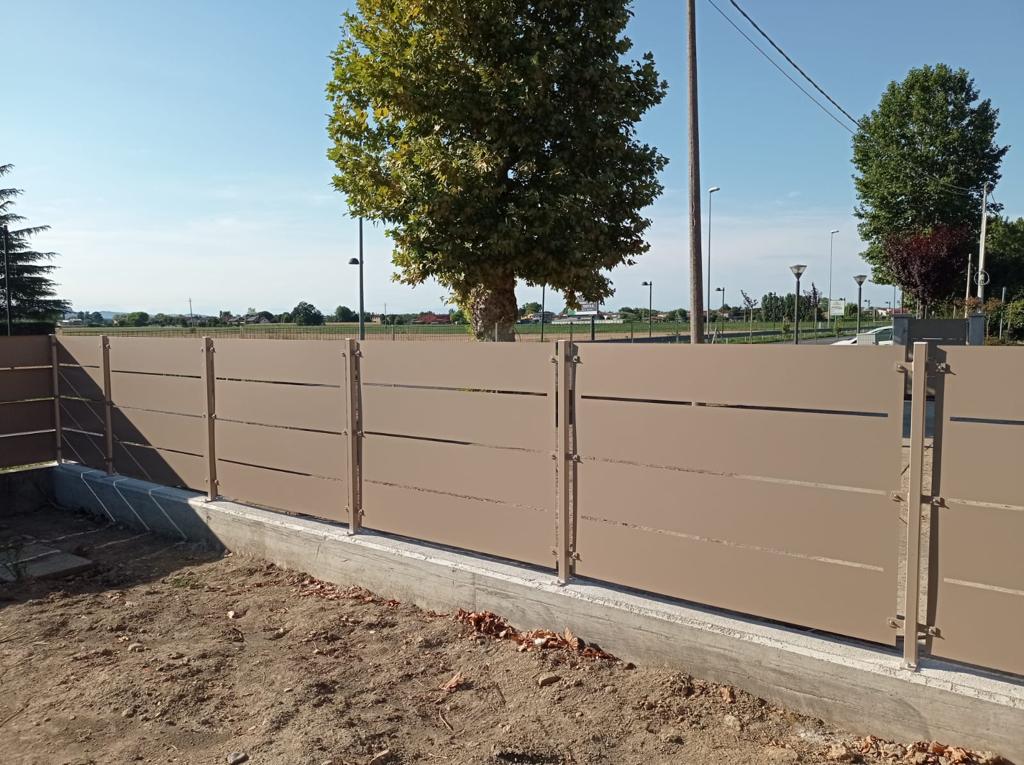 Recinzione in doghe orizzontali color marrone chiaro su base in cemento, pali con sommità decorative.