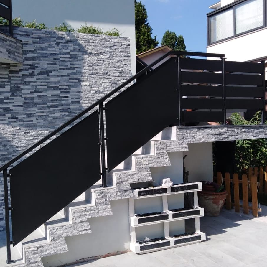 Ringhiera in metallo nero lungo le scale esterne con gradini in pietra e muro.