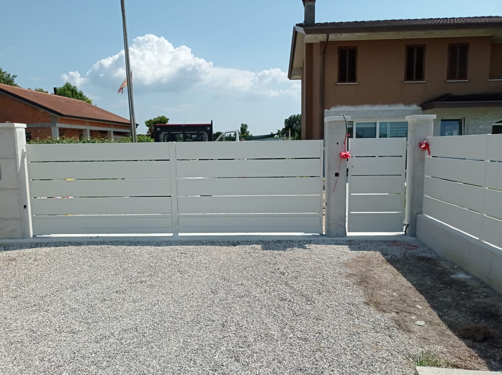 Recinzione bianca a doghe orizzontali con cancello scorrevole e cancello pedonale davanti a una casa.