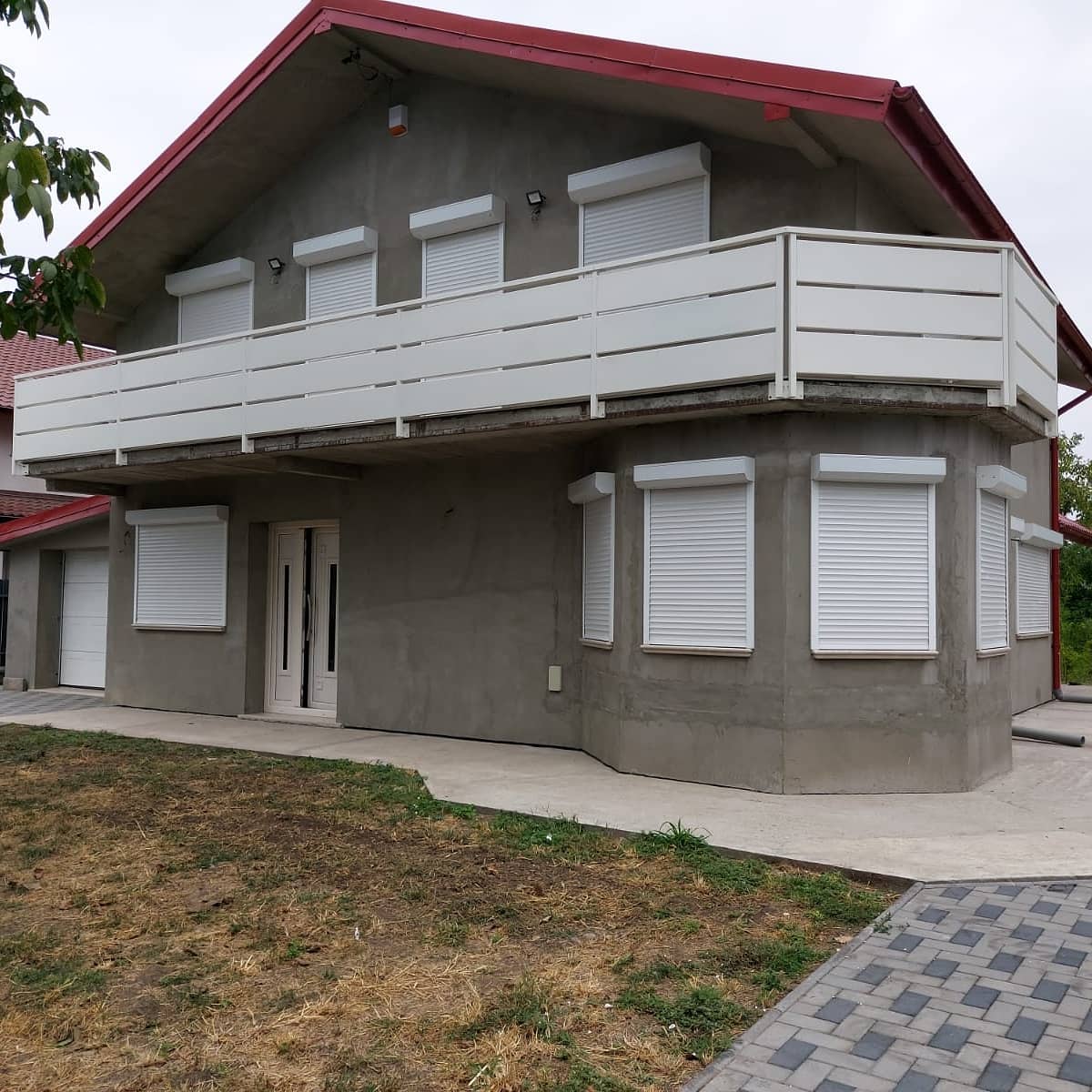 Casa a due piani con tetto rosso, persiane bianche, balcone ed esterno grigio.