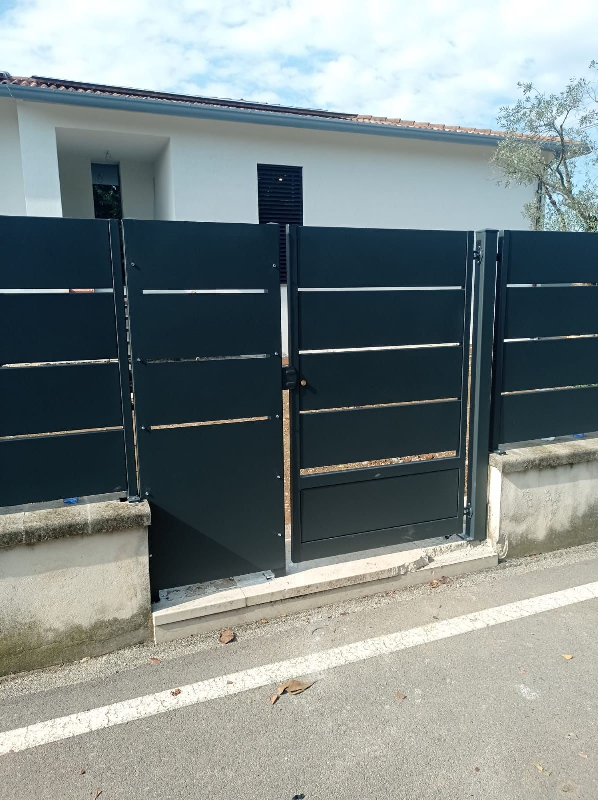 Cancello e recinzione in metallo nero di fronte a una casa bianca con cielo azzurro.