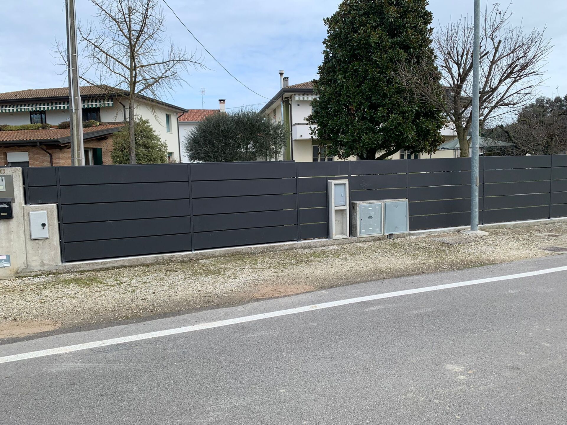 Recinzione orizzontale a doghe grigio scuro lungo una strada, di fronte agli edifici.