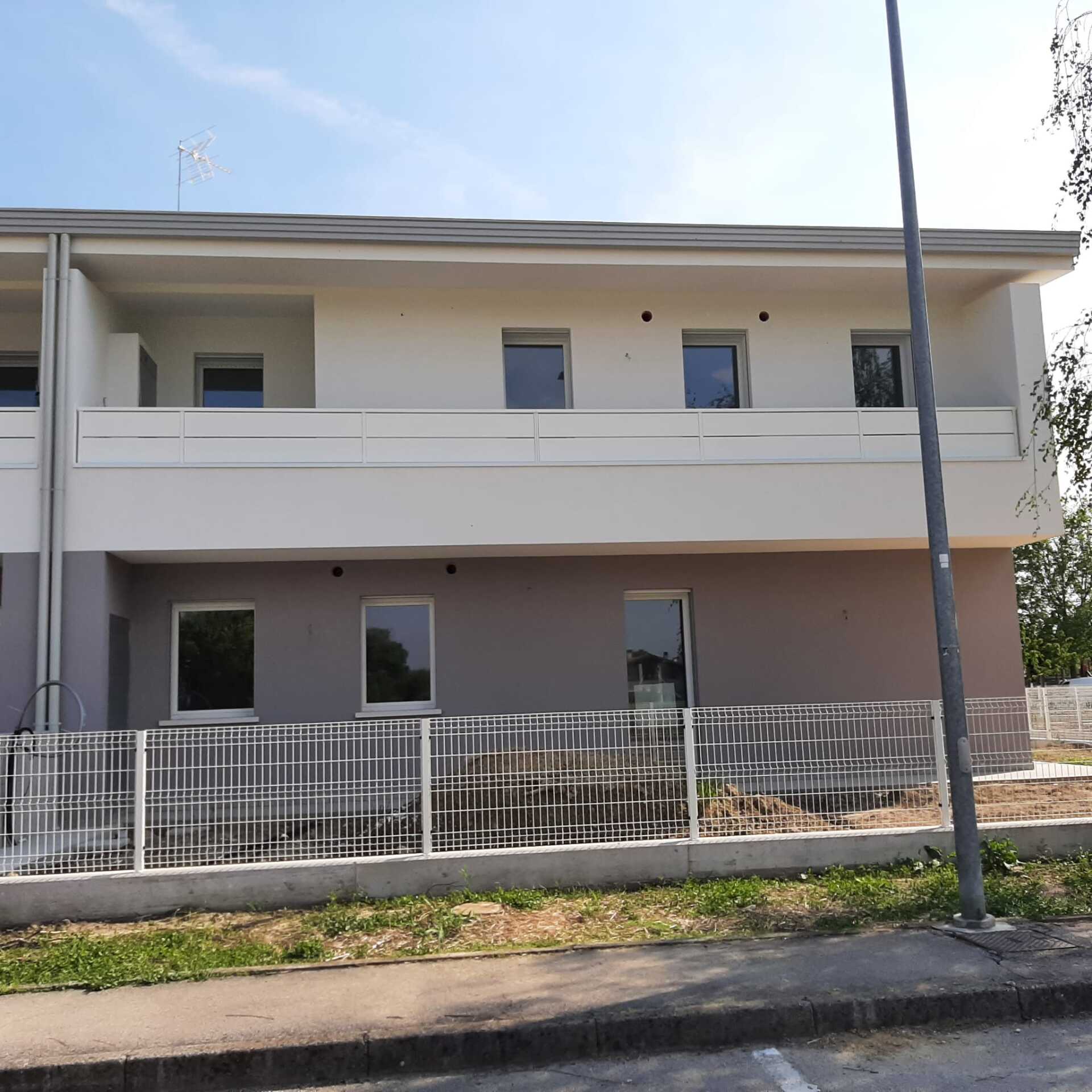 Casa a schiera a due piani con esterni di colore chiaro, finestre e una recinzione metallica decorativa lungo il marciapiede.