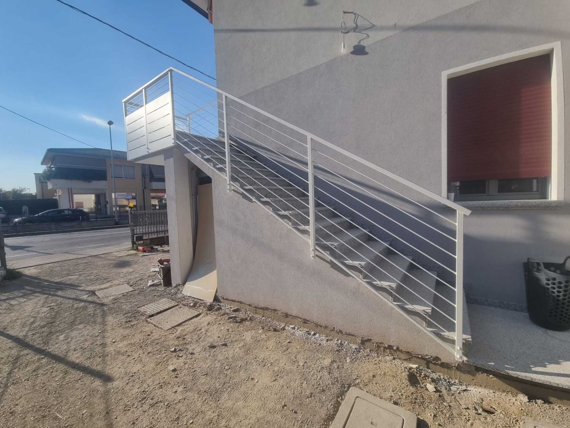 Scala esterna con ringhiera in metallo bianco contro un edificio grigio.