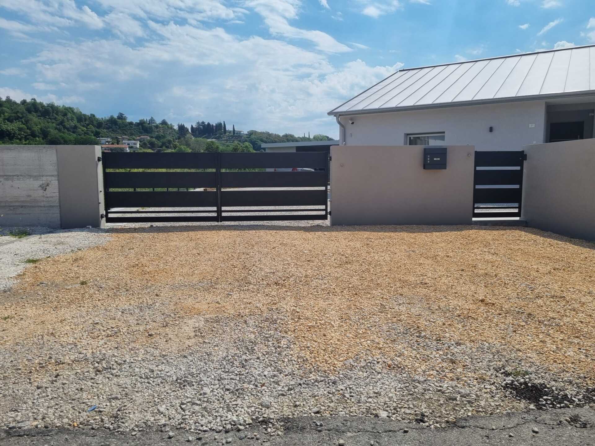 Una casa con un vialetto di ghiaia, un cancello di metallo e un piccolo cancello d'ingresso.