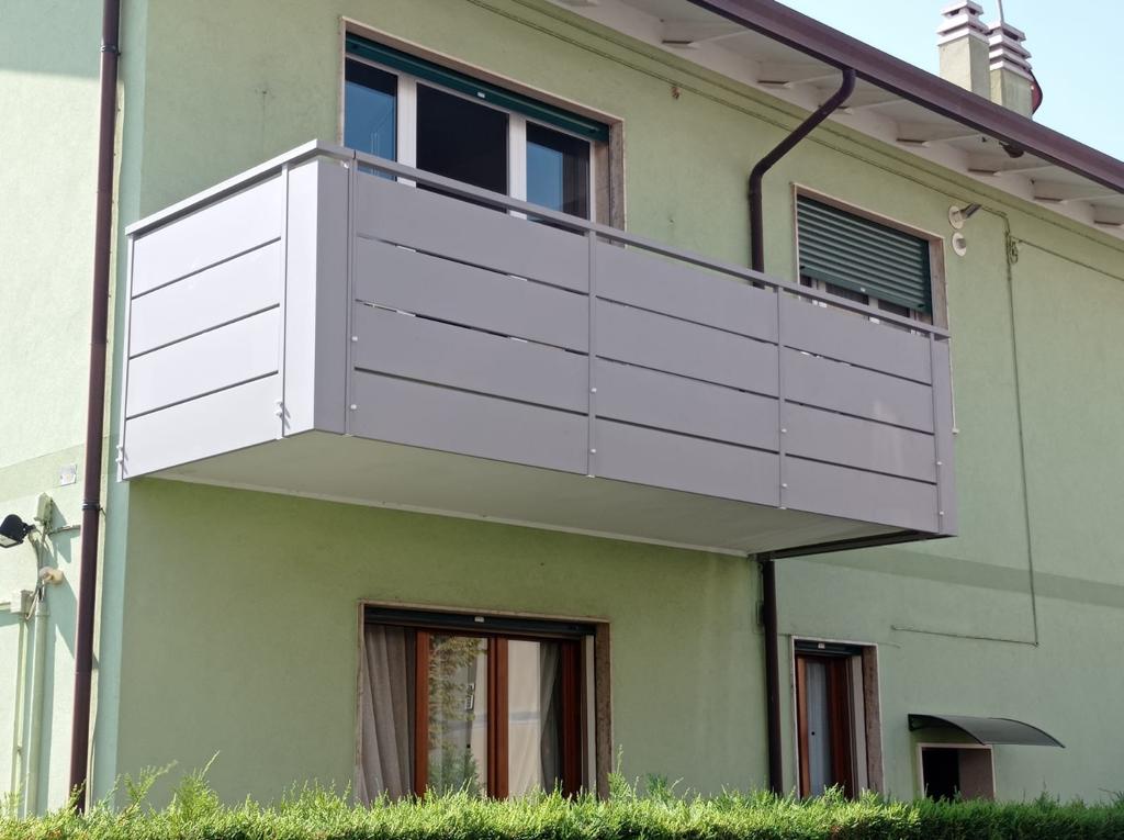 Balcone grigio su un edificio verde chiaro, con pannelli orizzontali.