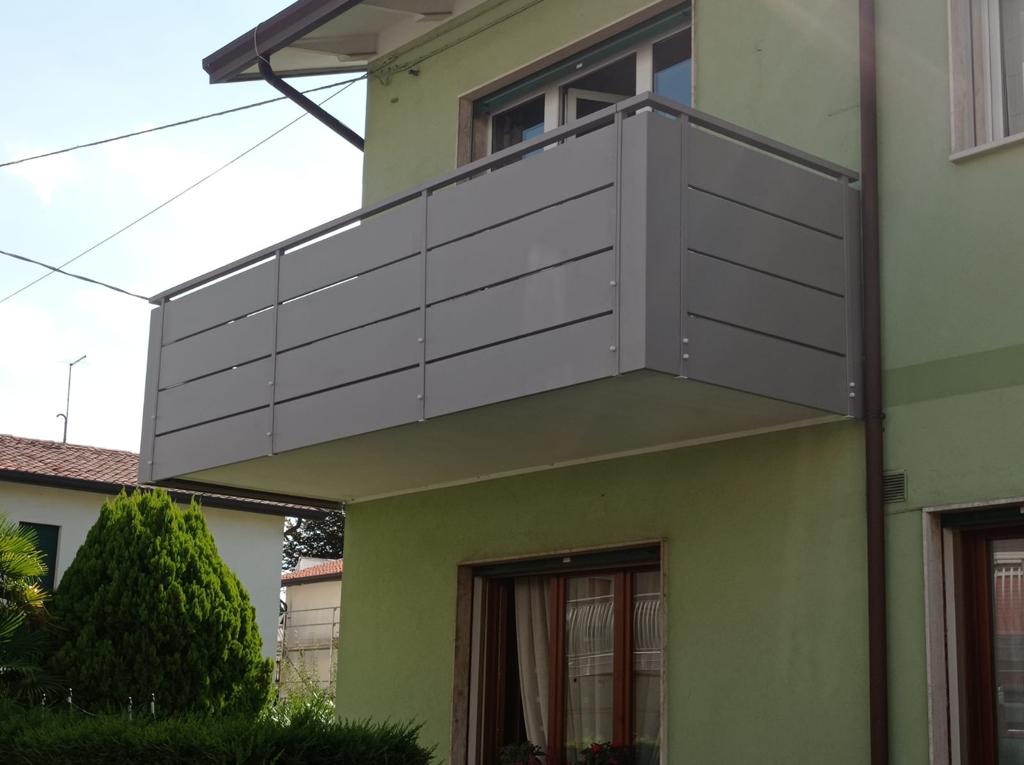 Balcone grigio su un edificio verde chiaro, con pannelli a doghe orizzontali.