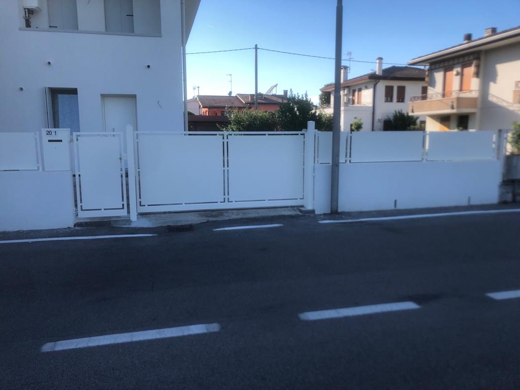 Casa bianca con cancello e muro bianchi lungo una strada.