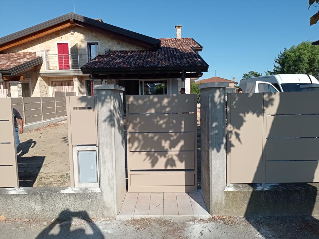 Cancello e recinzione beige davanti a una casa, con una piccola porticina per animali domestici e pilastri di cemento.