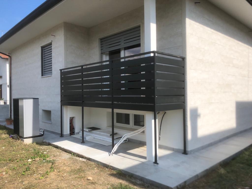 Ringhiera del balcone con listelli neri in una casa moderna con esterni chiari e prato verde.