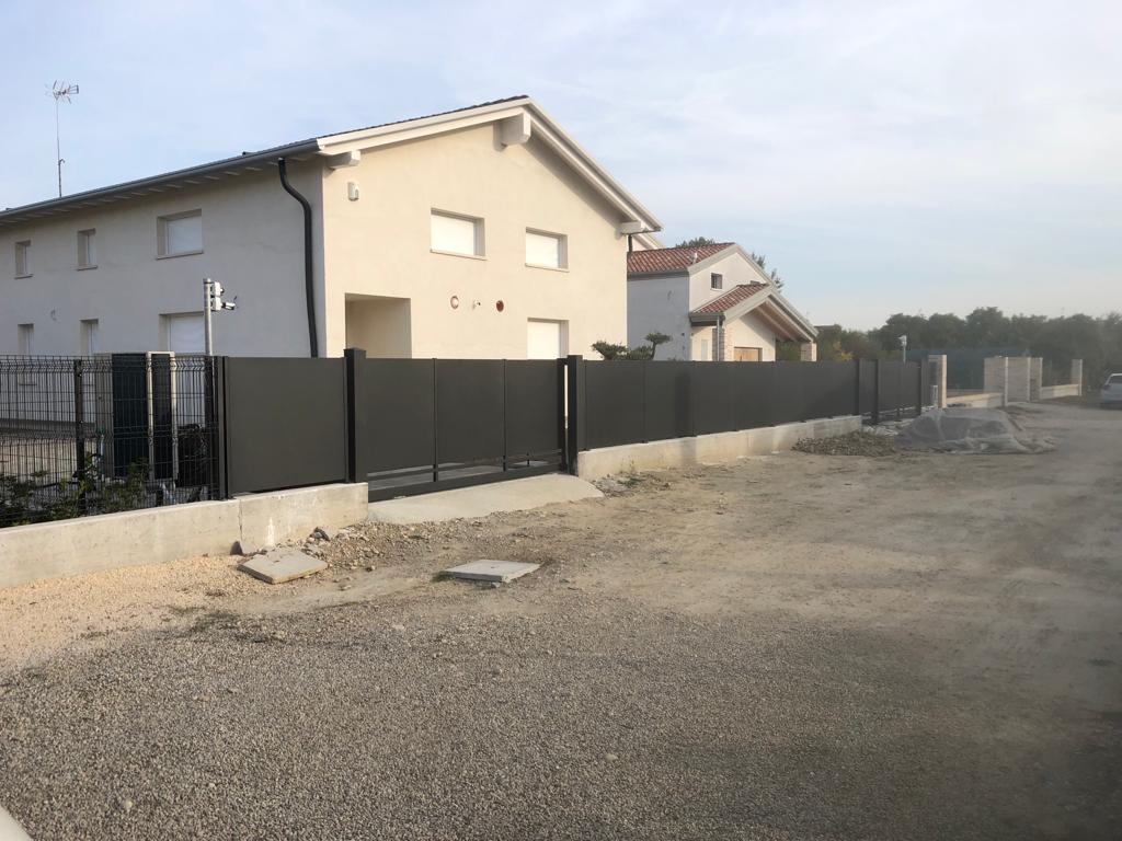 Casa grigia dietro una recinzione grigio scuro con base in cemento e vialetto di ghiaia.