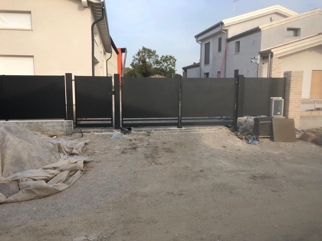 Cancello e recinzione in metallo nero davanti alle case a due piani; materiali da costruzione visibili.