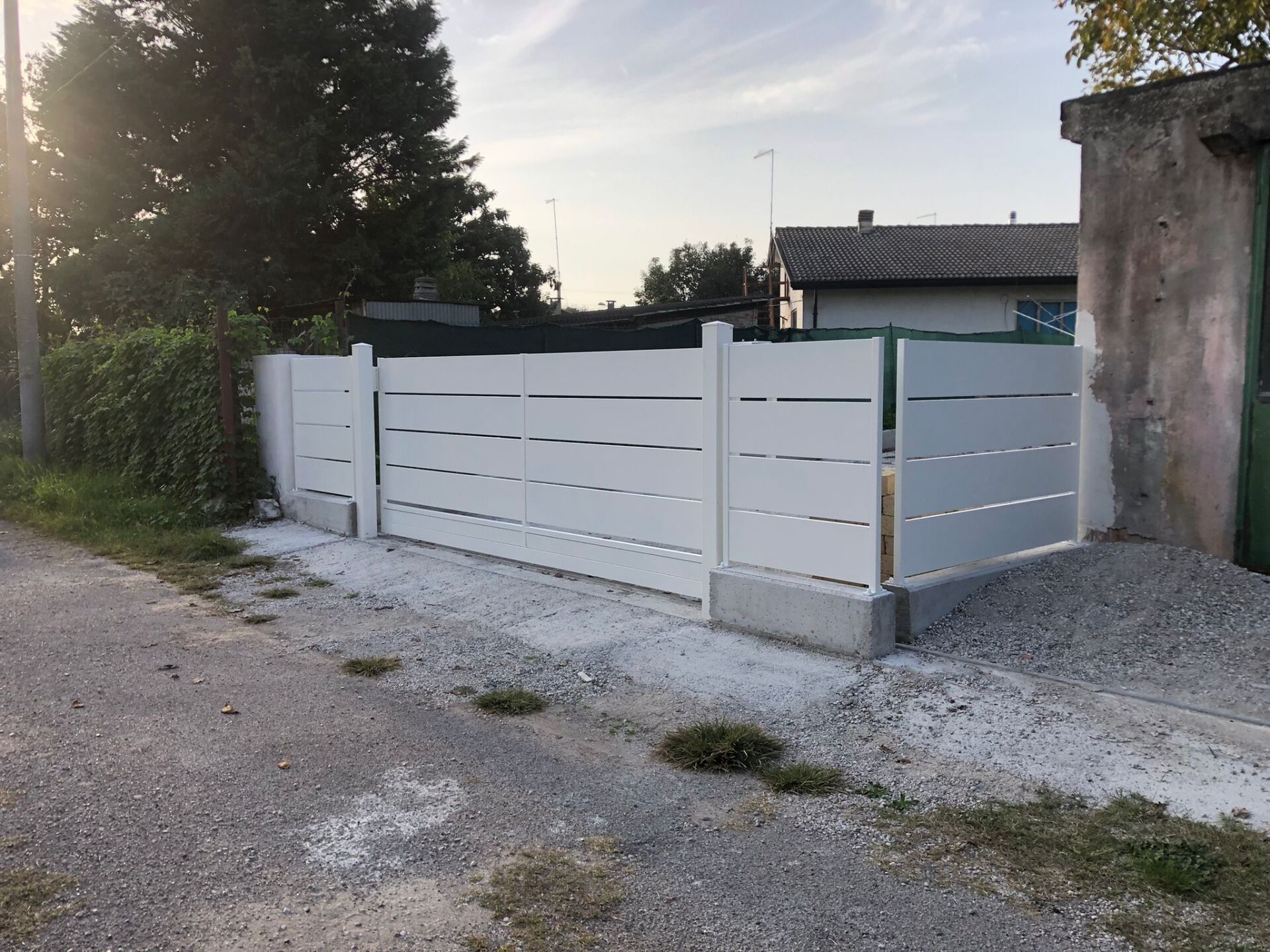 Recinzione bianca con listelli orizzontali e vialetto in ghiaia.