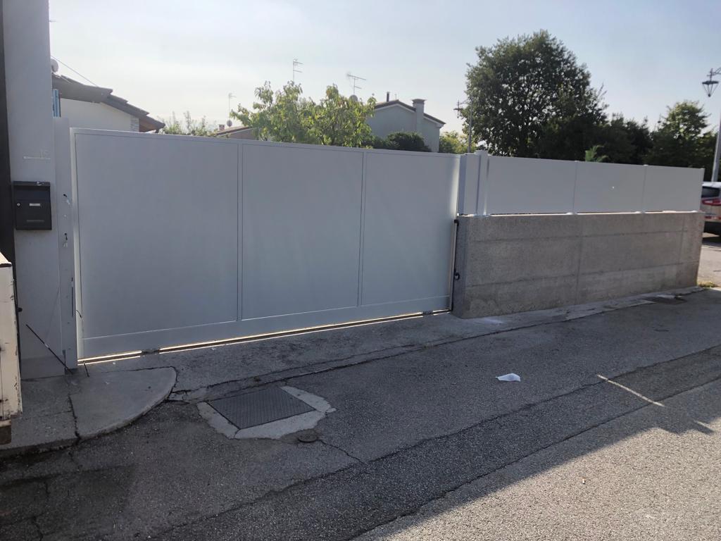 Cancello scorrevole grigio davanti a un edificio, su una strada asfaltata.