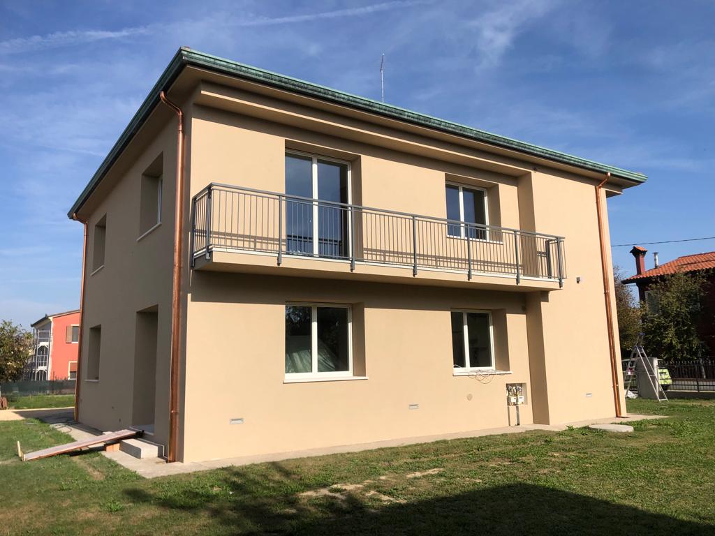 Casa beige a due piani con balcone e ringhiera in metallo, contro un cielo azzurro.