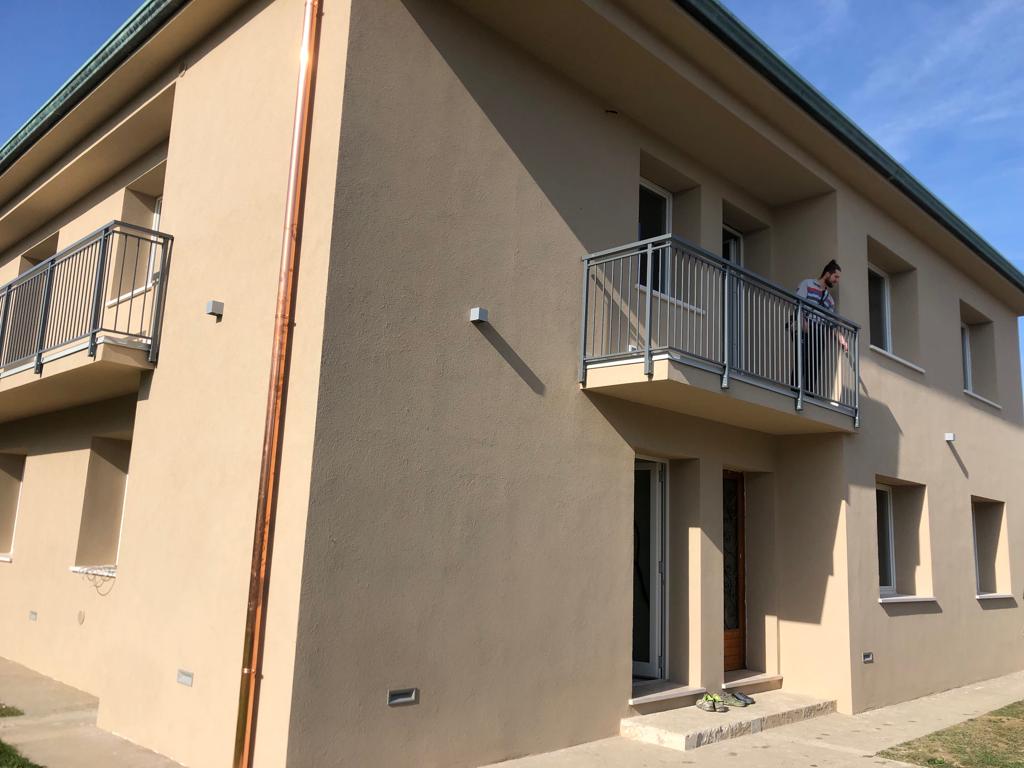 Edificio beige a due piani con un balcone e una persona in piedi su di esso.