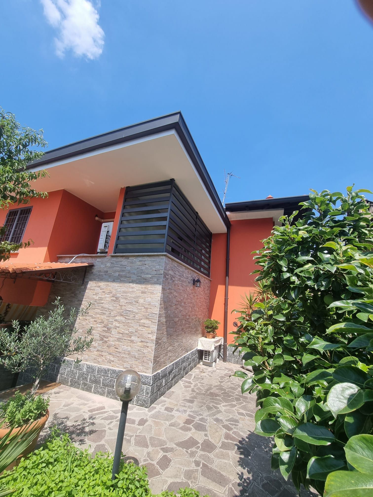 Casa in stucco arancione con facciata in pietra, tetto scuro e veranda coperta in una giornata di sole.