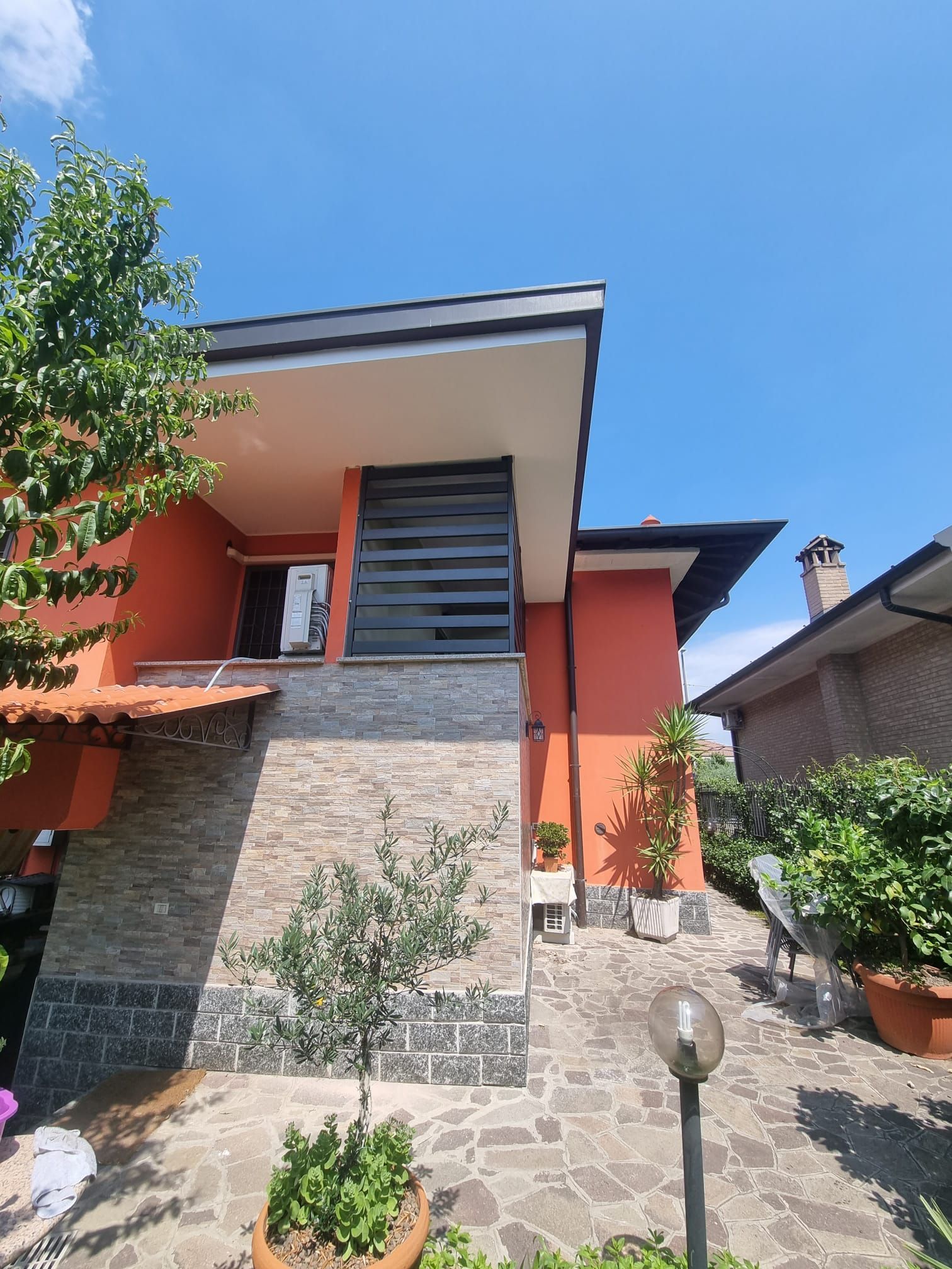 Casa arancione a due piani con dettagli in pietra, alberi e cielo azzurro.