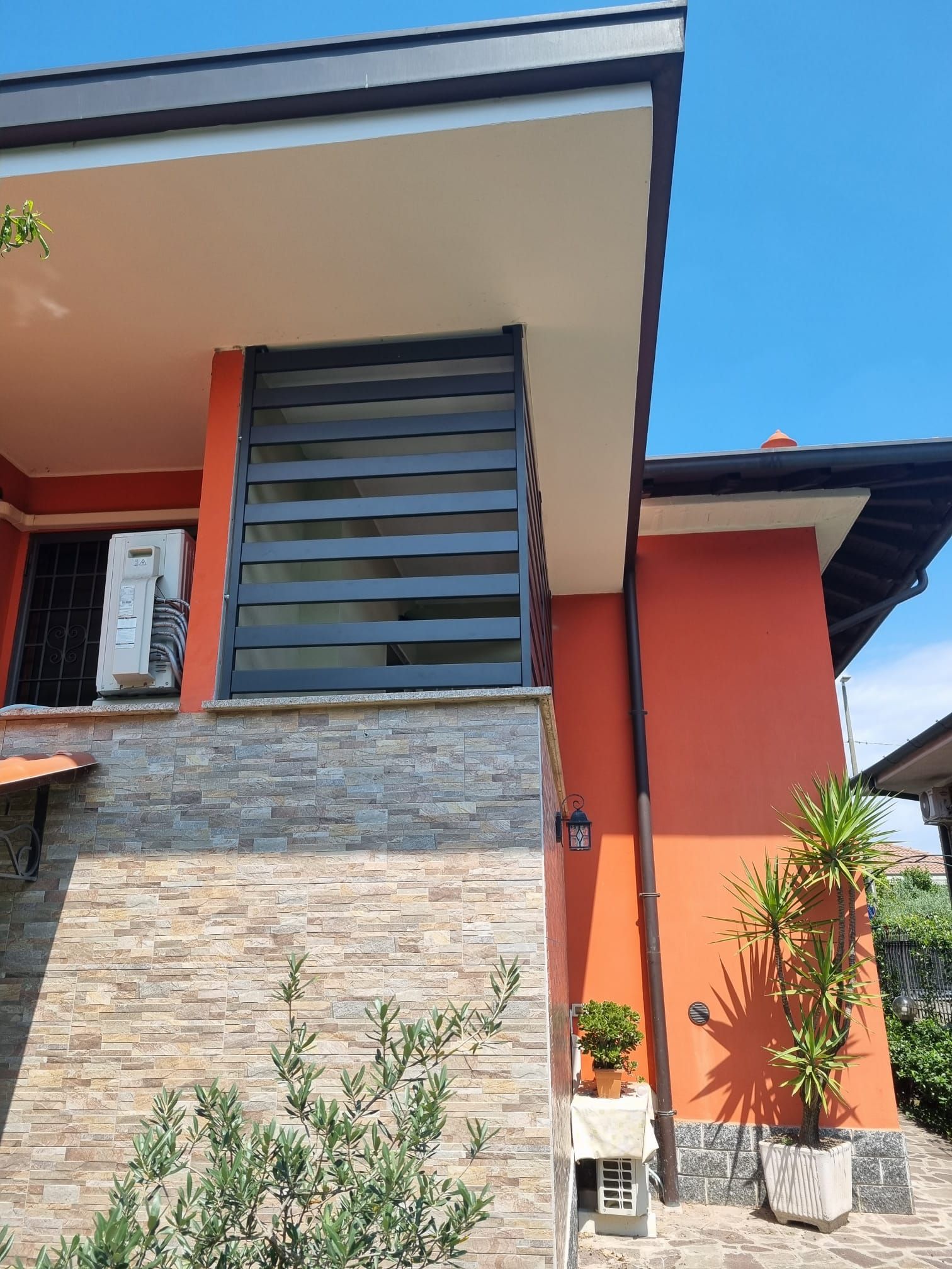 Esterno della casa in pietra e arancione con una tenda per la privacy a doghe nere sul portico.