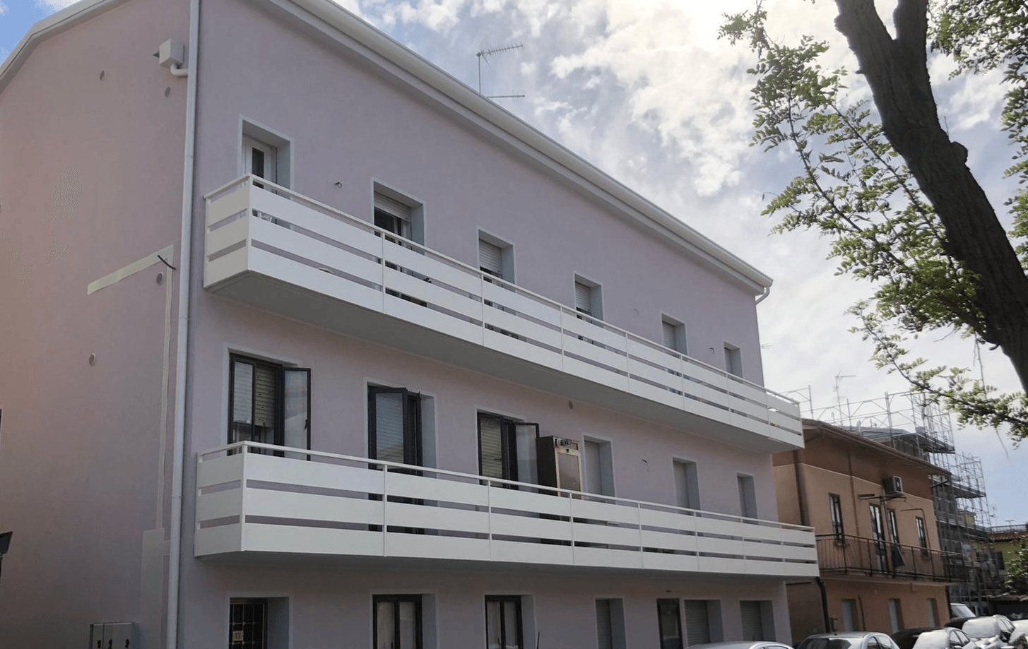 Edificio viola chiaro con balconi e finiture bianche sotto un cielo nuvoloso.