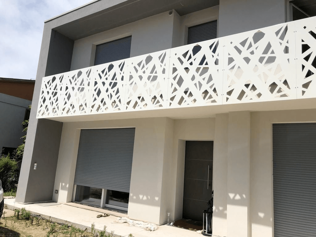 Moderna casa bianca con intricata ringhiera del balcone tagliata al laser. Tapparelle e porta grigia.