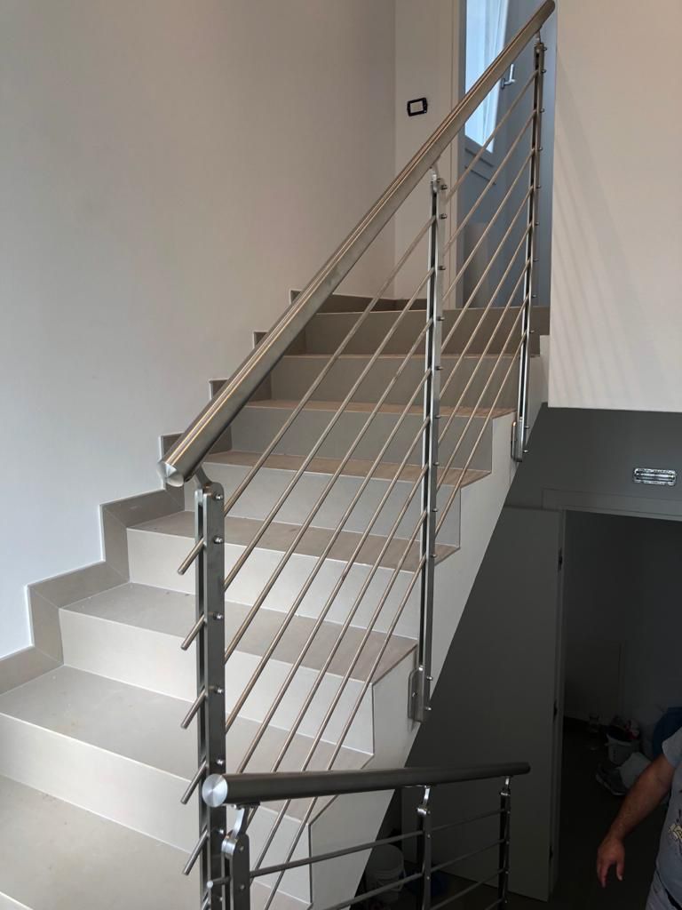 Scala con moderna ringhiera in acciaio inox e riempimento tramite cavi, che sale contro una parete bianca.