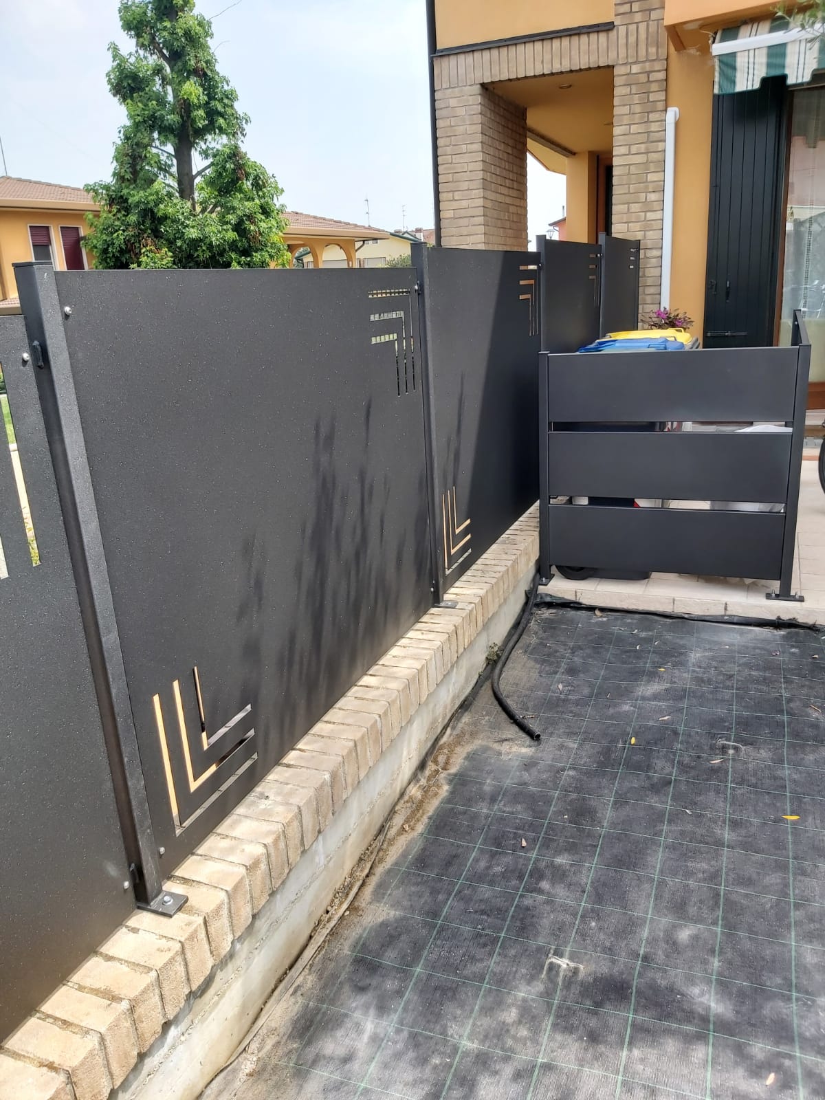 Recinzione in metallo nero con ritagli decorativi, posta su una base in mattoni all'esterno.