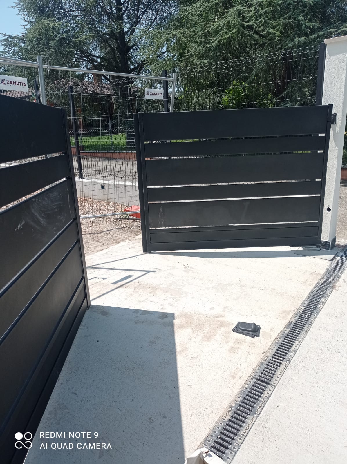 Cancello carrabile in metallo nero, aperto, su superficie in cemento, con grata.