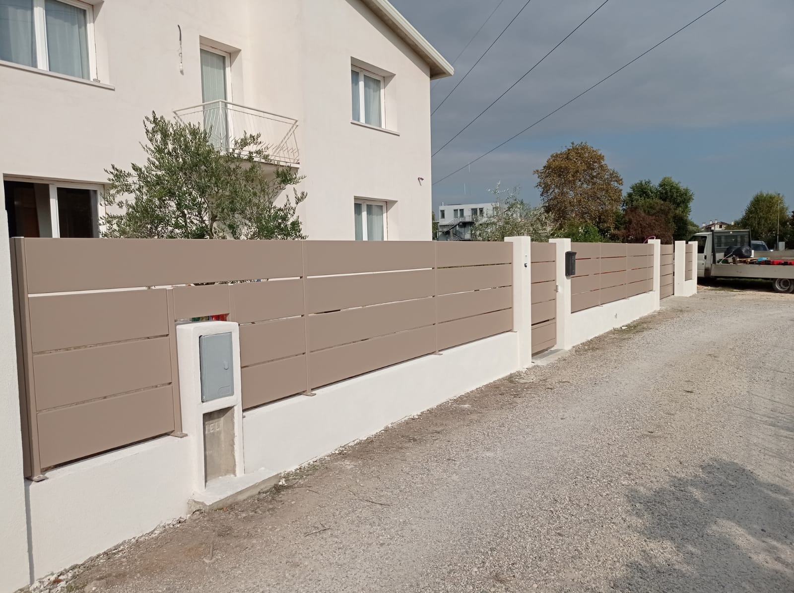 Recinzione orizzontale beige davanti a una casa chiara su un vialetto di ghiaia.