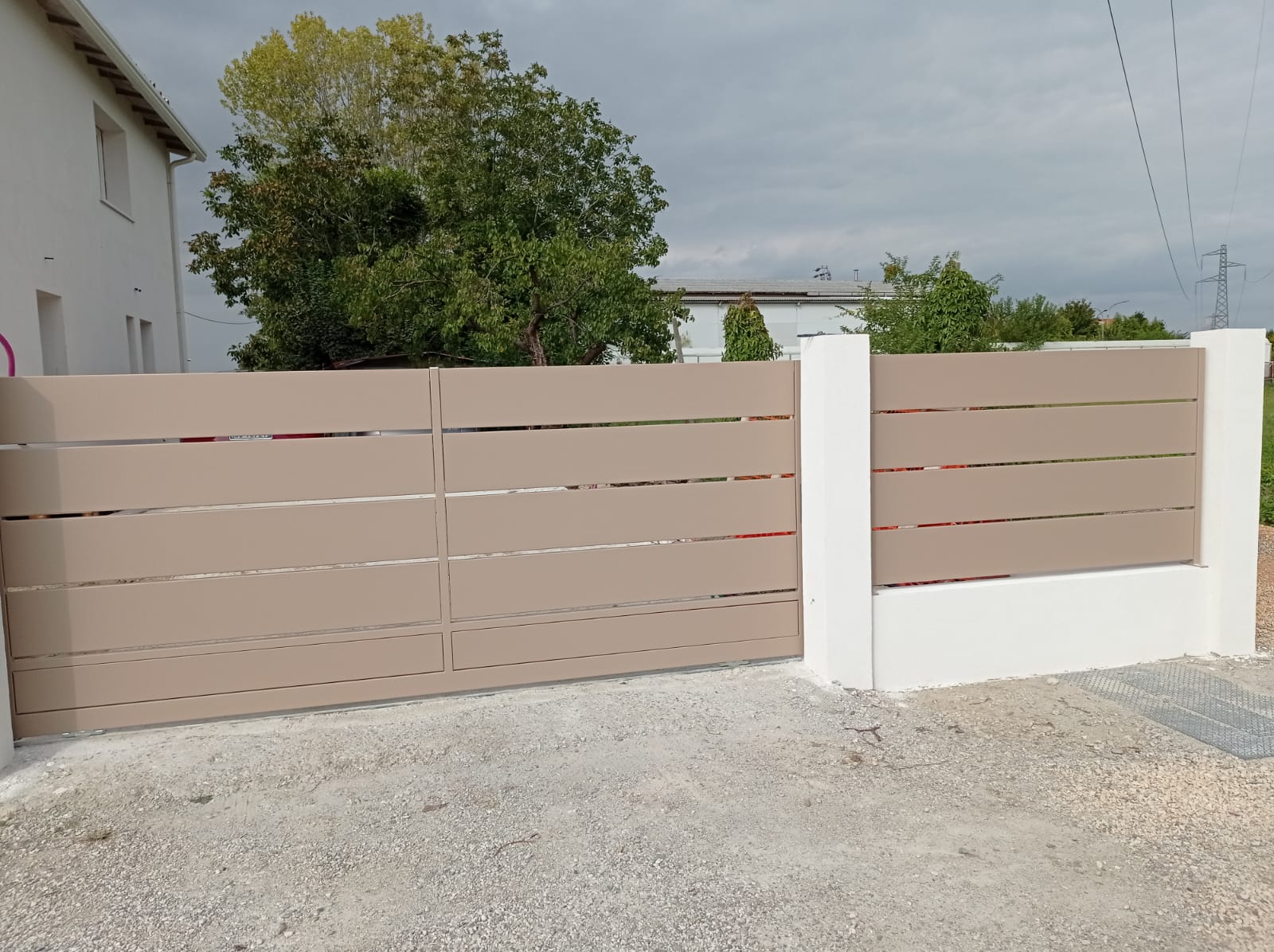 Recinzione orizzontale in doghe color marrone chiaro con pali bianchi e cancello davanti a una casa.