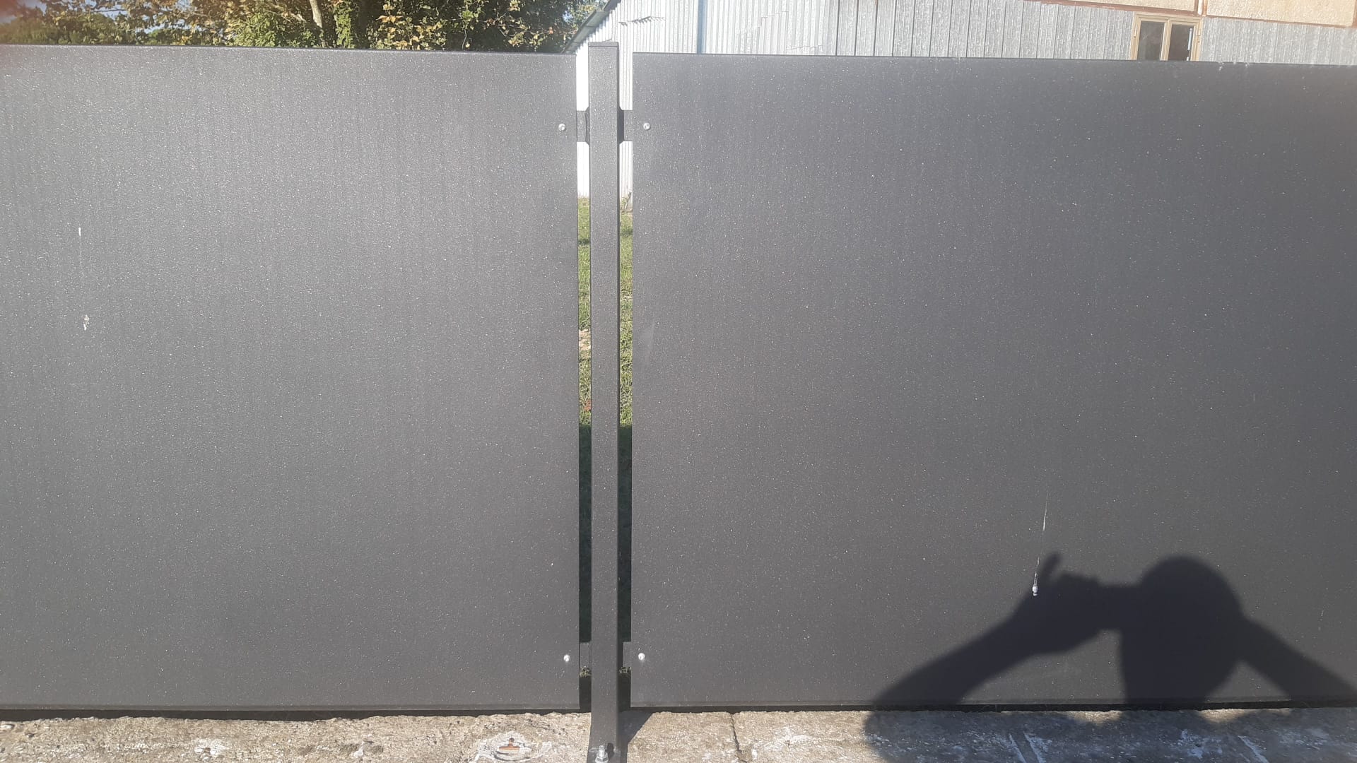Recinzione in metallo grigio, due pannelli con uno spazio al centro. La luce del sole proietta un'ombra.