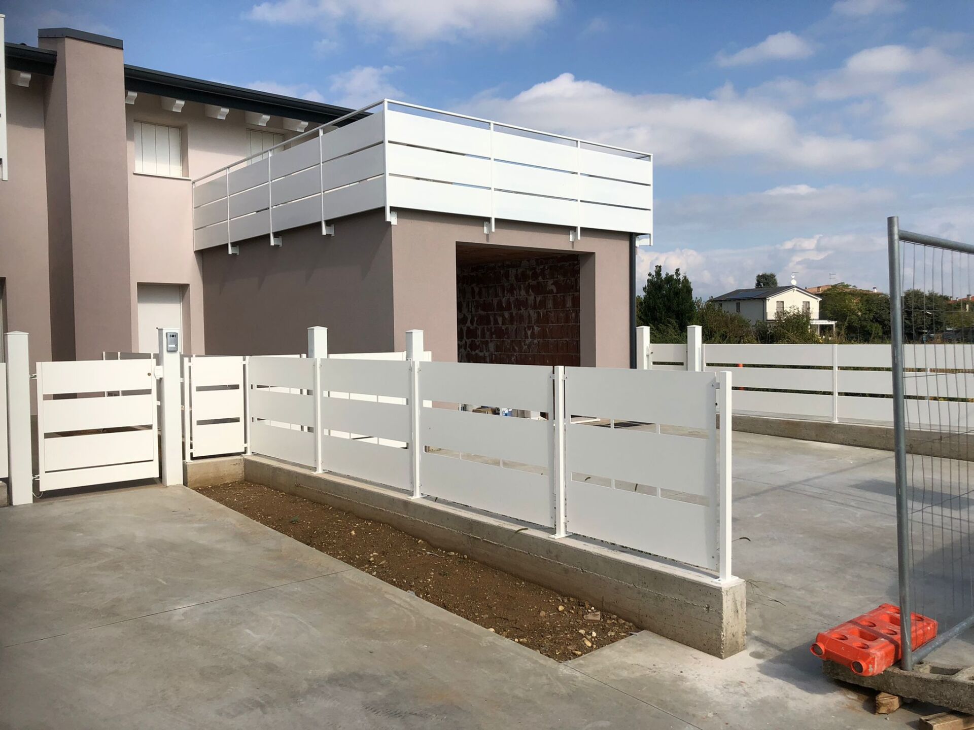 Recinzione e cancello in doghe bianche che circondano una casa moderna con balcone al secondo piano in una giornata di sole.