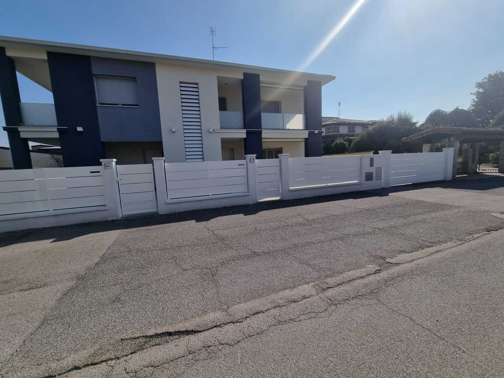 Recinzione bianca davanti a un edificio a due piani con facciata blu scuro e bianca, sotto un cielo luminoso.