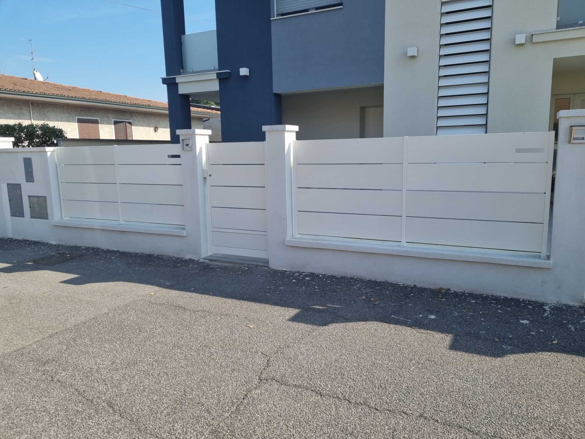 Recinzione bianca con listelli orizzontali e cancello davanti a una casa moderna, giornata di sole.
