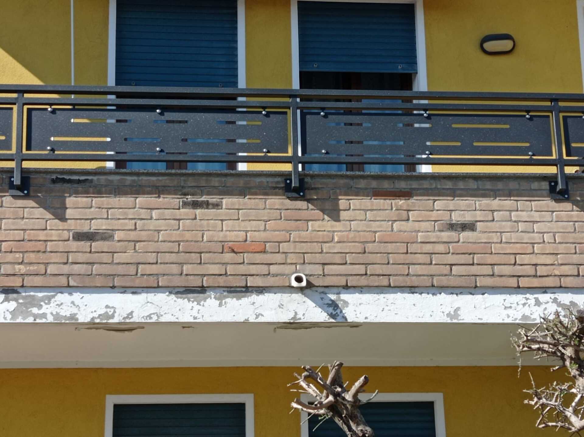 Balcone con ringhiera nera, muro di mattoni e facciata gialla dell'edificio.