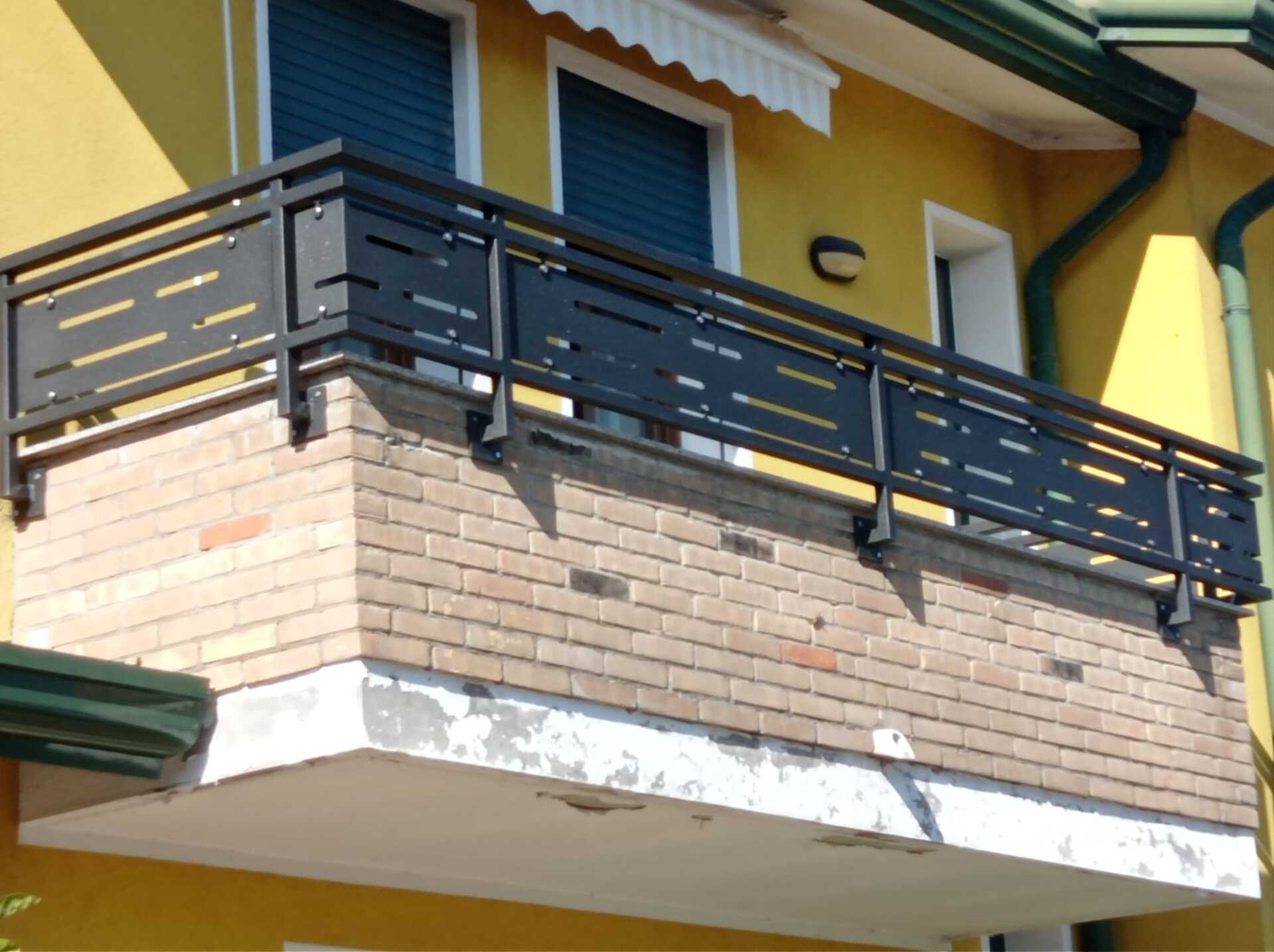 Ringhiera in metallo nero per balcone su una sporgenza in mattoni attaccata a un edificio giallo.