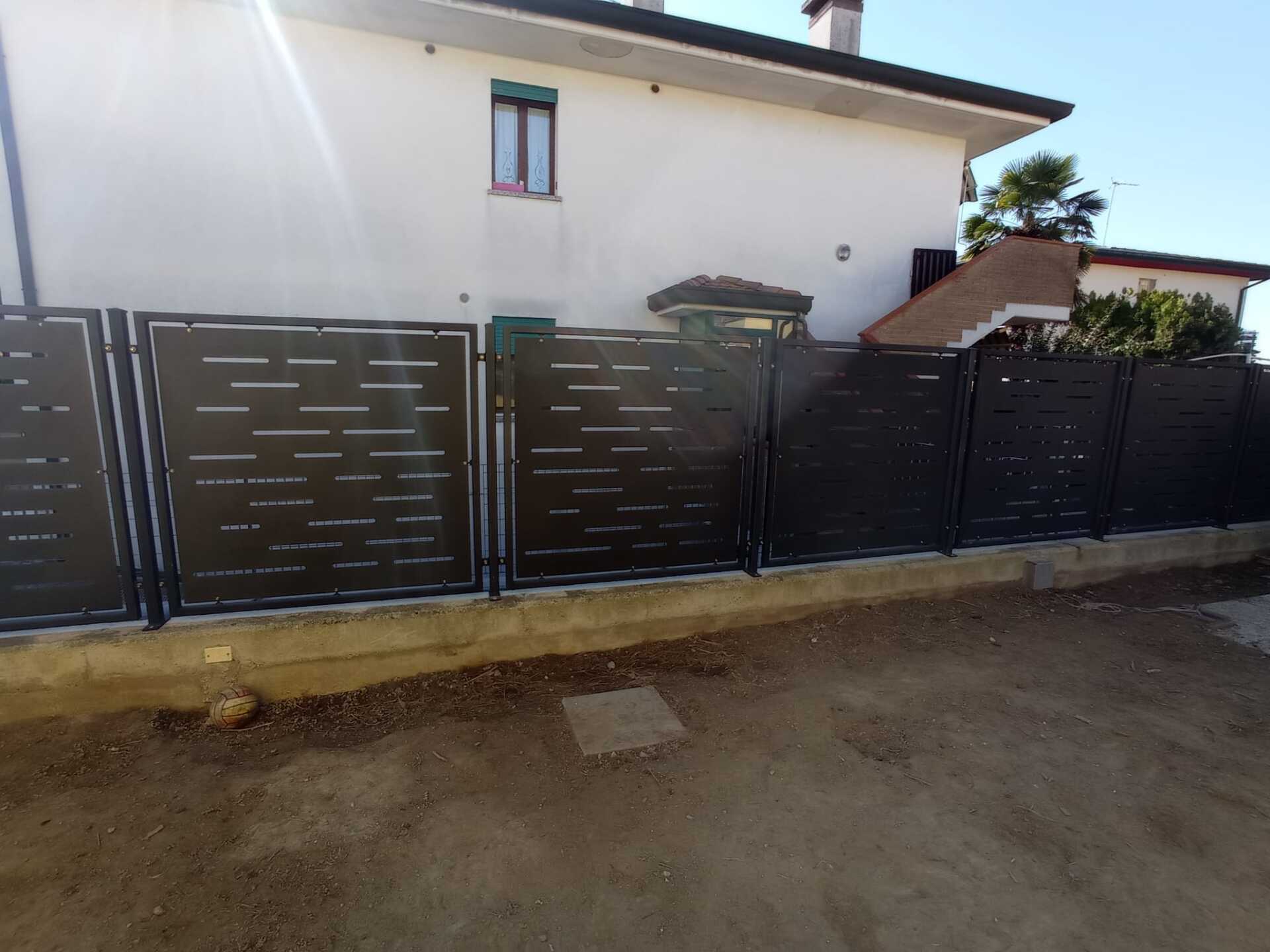 Recinzione in metallo nero davanti a una casa bianca con vialetto in terra battuta e ghiaia.