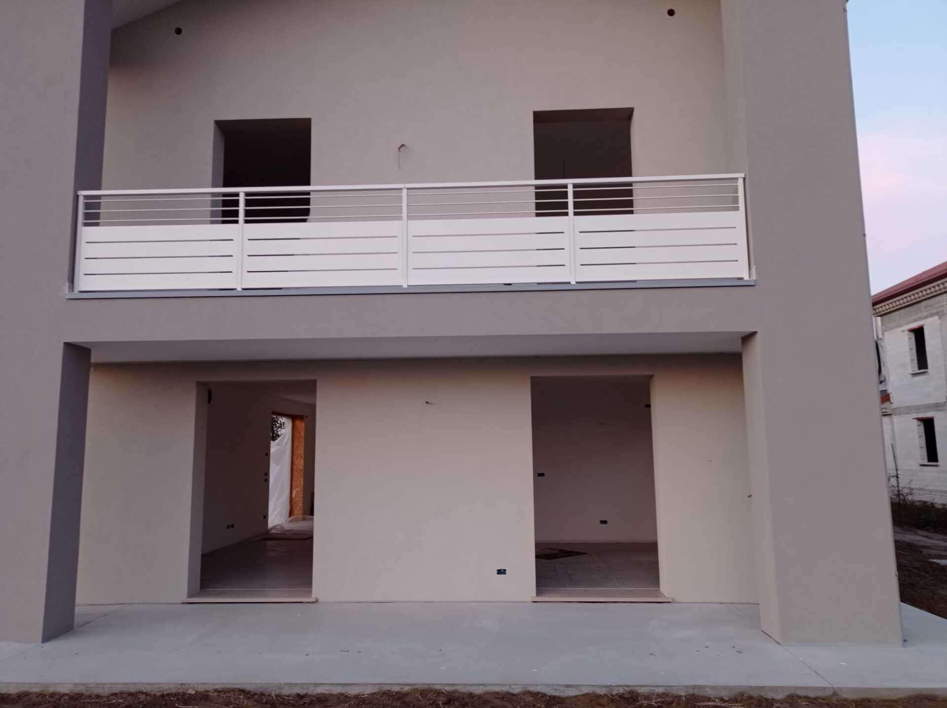 Esterno di una casa a due piani con pareti grigie, ringhiera bianca del balcone e porte aperte.