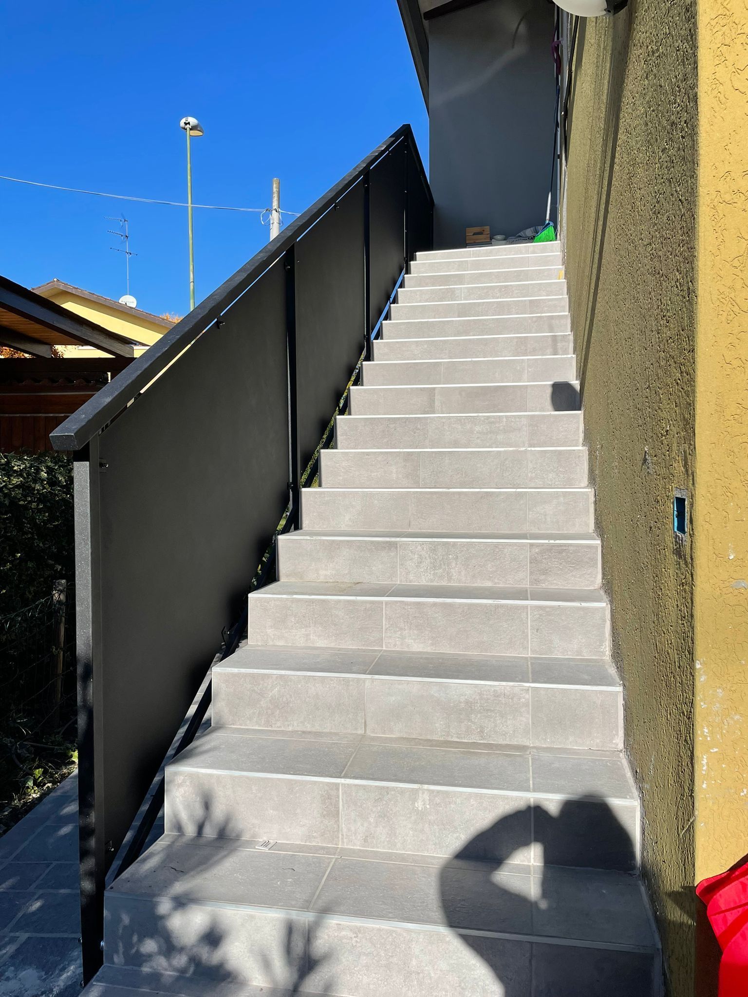 Scala esterna con gradini in piastrelle grigie, ringhiera nera e parete gialla.