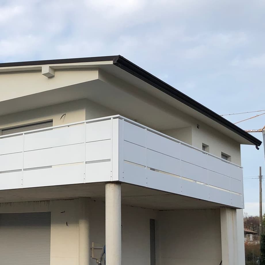 Moderno edificio a due piani con balcone bianco e tetto grigio, sotto un cielo nuvoloso.