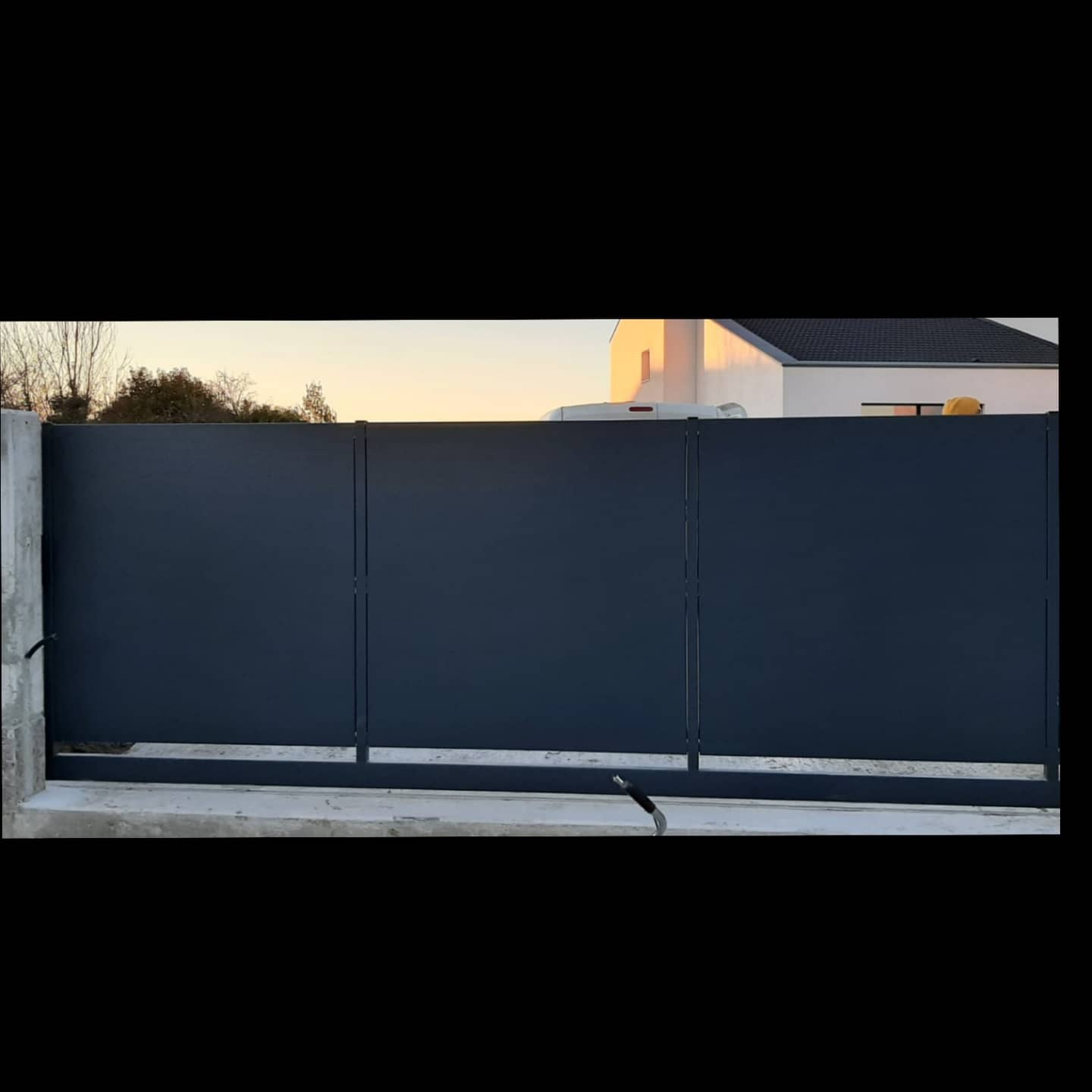 Cancello scorrevole in metallo blu scuro davanti a una casa.