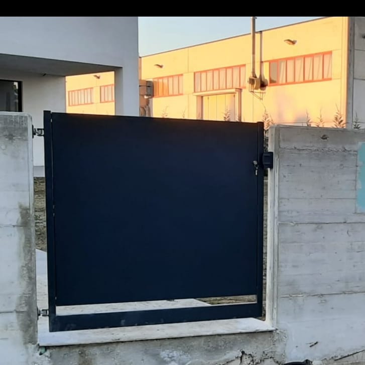 Cancello in metallo nero con struttura in cemento, all'esterno di un edificio con illuminazione calda.