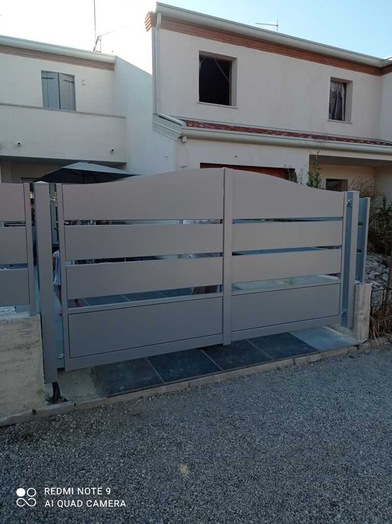 Cancello di metallo grigio davanti a una casa bianca con vialetto di ghiaia.