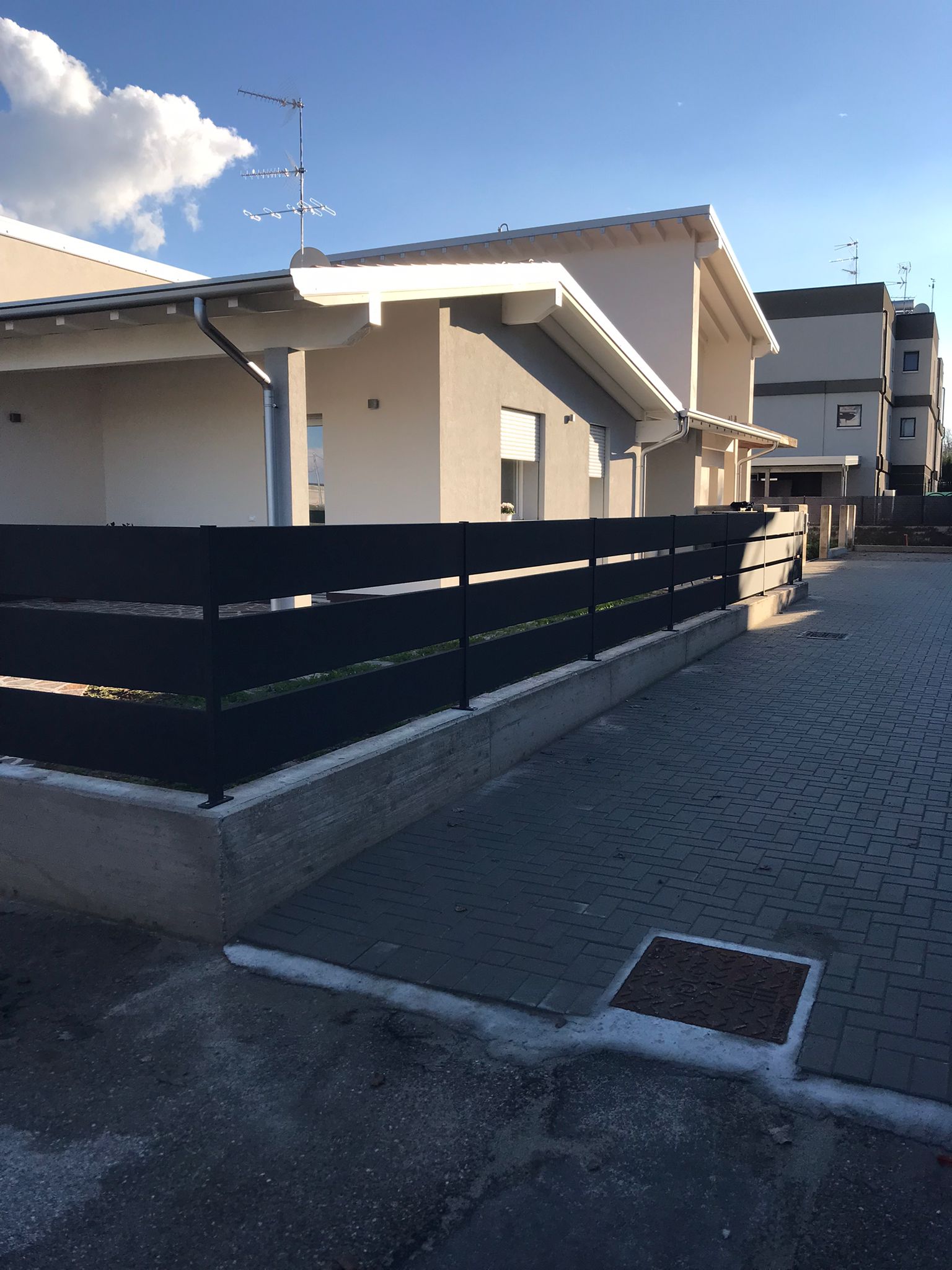 Casa moderna con recinzione nera e vialetto pavimentato in una giornata di sole.