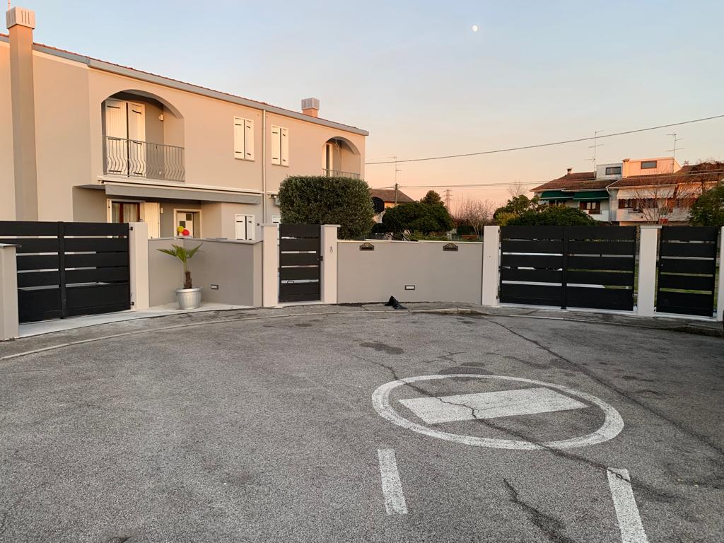 Casa grigia con cancelli neri, vialetto d'accesso e un simbolo circolare del traffico dipinto.